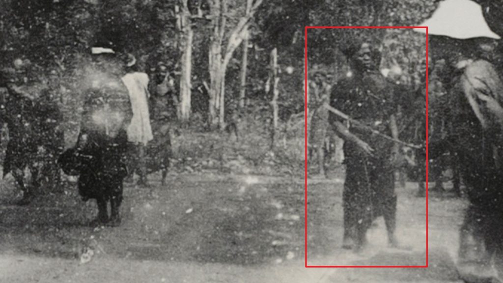 A police officer caught in the background of a panoramic photograph taken during Northcote Thomas's 1910-11 tour of Awka District